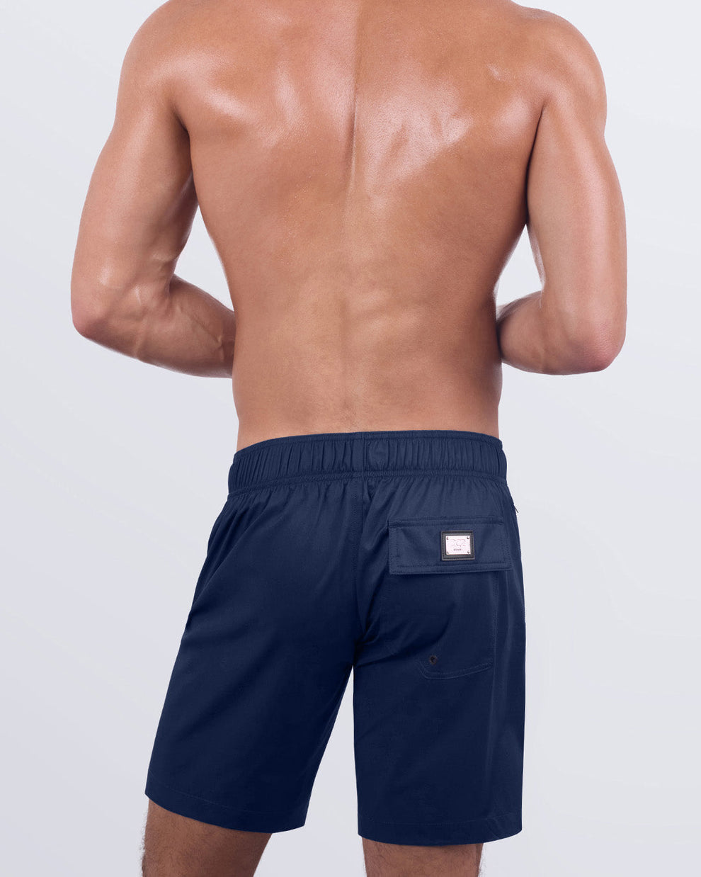 Back view of a male model wearing the NAVY BOOMER Flex Boardshorts by DC2 Miami. These stylish boardshorts showcase a sleek, tailored fit with a functional back pocket featuring the DC2 signature metal logo plaque, a secure flap closure, and breathable water-resistant fabric designed for all-day comfort.