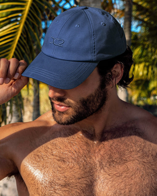 DC2 Navy Blue Resort Cap — model wearing navy blue men’s baseball cap with embroidered DC2 logo in a tropical setting.