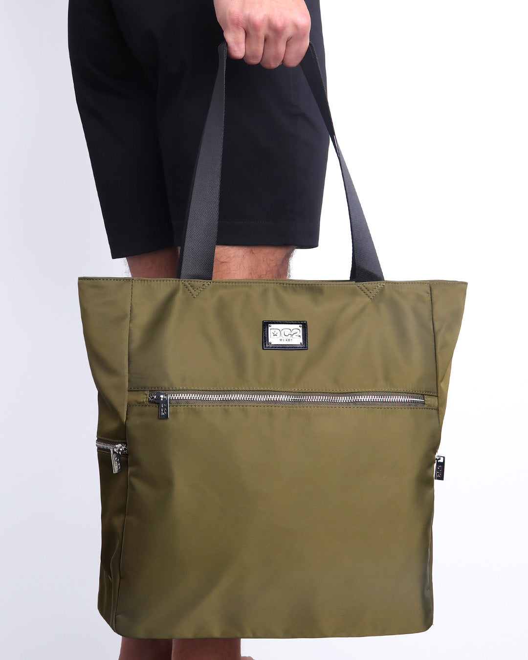 Side view of the PALM GREEN Poolside Tote Bag Foldable/Portable by DC2 brand. Features smooth zipper in the front and the side, water resistant fabric, and the DC2 logo in a metallic silver plaque.