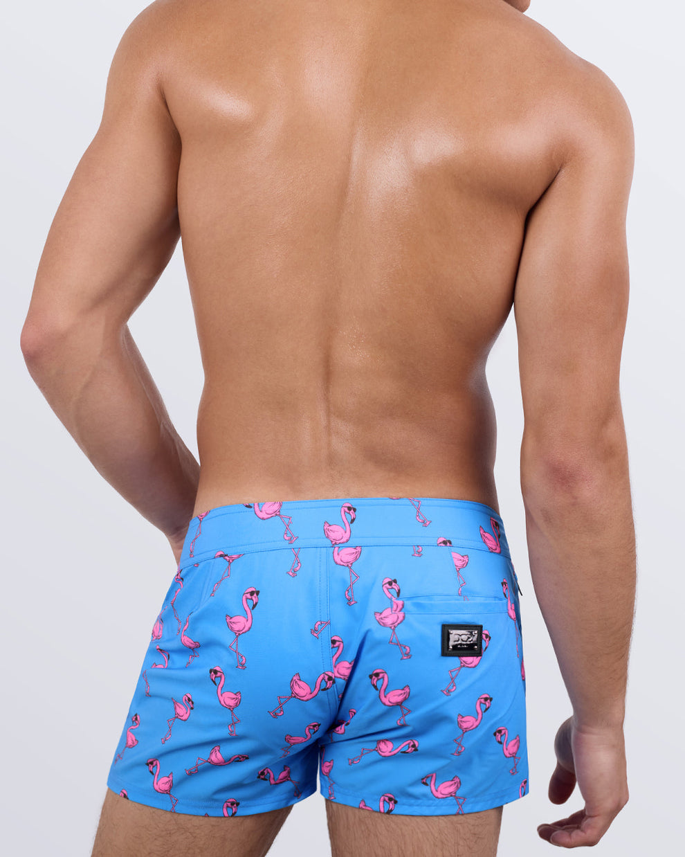 Back view of a male model wearing the men's PINK FLAMINGOS beach shorts by DC2 Miami. Featuring a fun and stylish flamingo print, a sleek fit, and a functional back pocket with a DC2 signature metal logo plaque, these premium swim shorts combine eye-catching design with ultimate comfort.