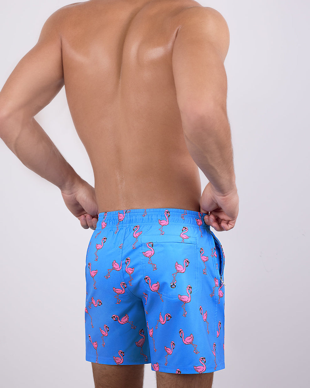 Back view of a male model wearing the PINK FLAMINGOS Resort Shorts by DC2 Miami. These resort-style swim shorts showcase a tailored, long-leg cut, a functional back pocket.