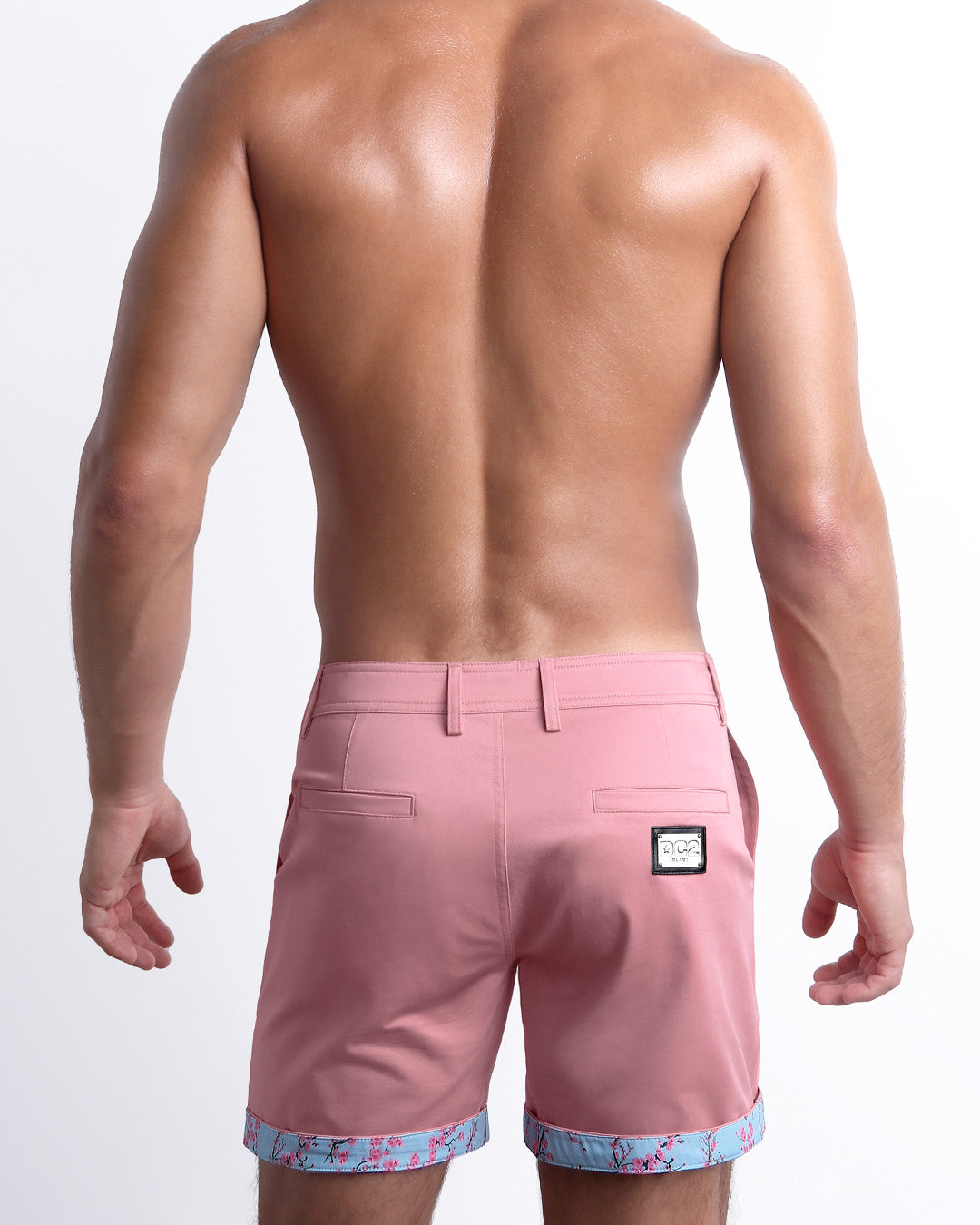 Back view of a model wearing woven twill cotton chino shorts in a light pink color for men. These premium quality swimwear bottoms are DC2 by BANG! Clothes, a men’s beachwear brand from Miami.