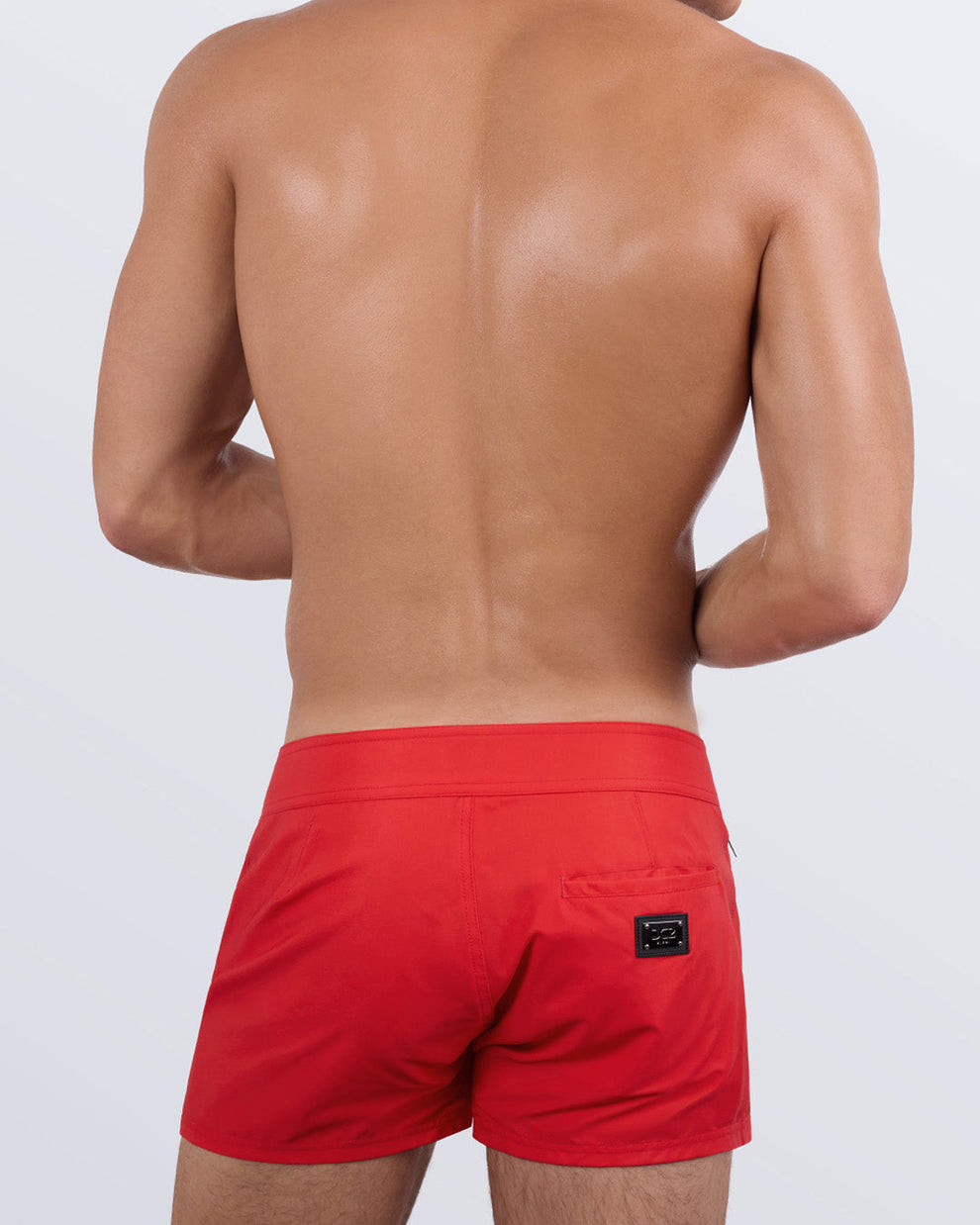 Back view of a male model wearing men’s beach trunks in red color by the DC2 Miami Clothes brand of men's beachwear.