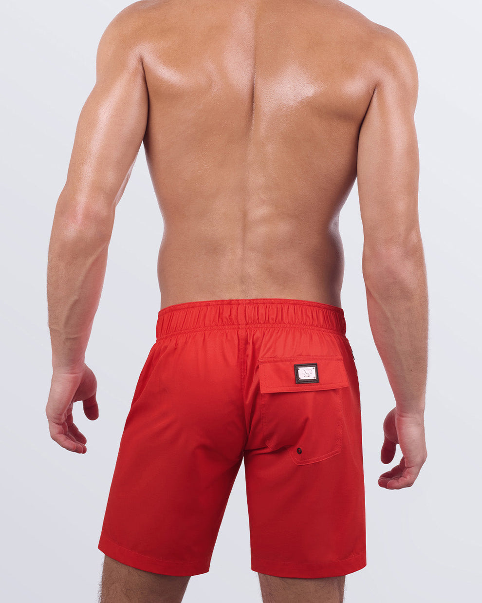 Back view of a male model wearing the PRIME RED Flex Boardshorts by DC2 Miami. These stylish boardshorts include a functional back pocket with a flap closure, a DC2 signature metal logo plaque, and an elasticated back waistband for enhanced flexibility and comfort. The quick-dry fabric and breathable lining make them ideal for all-day wear.
