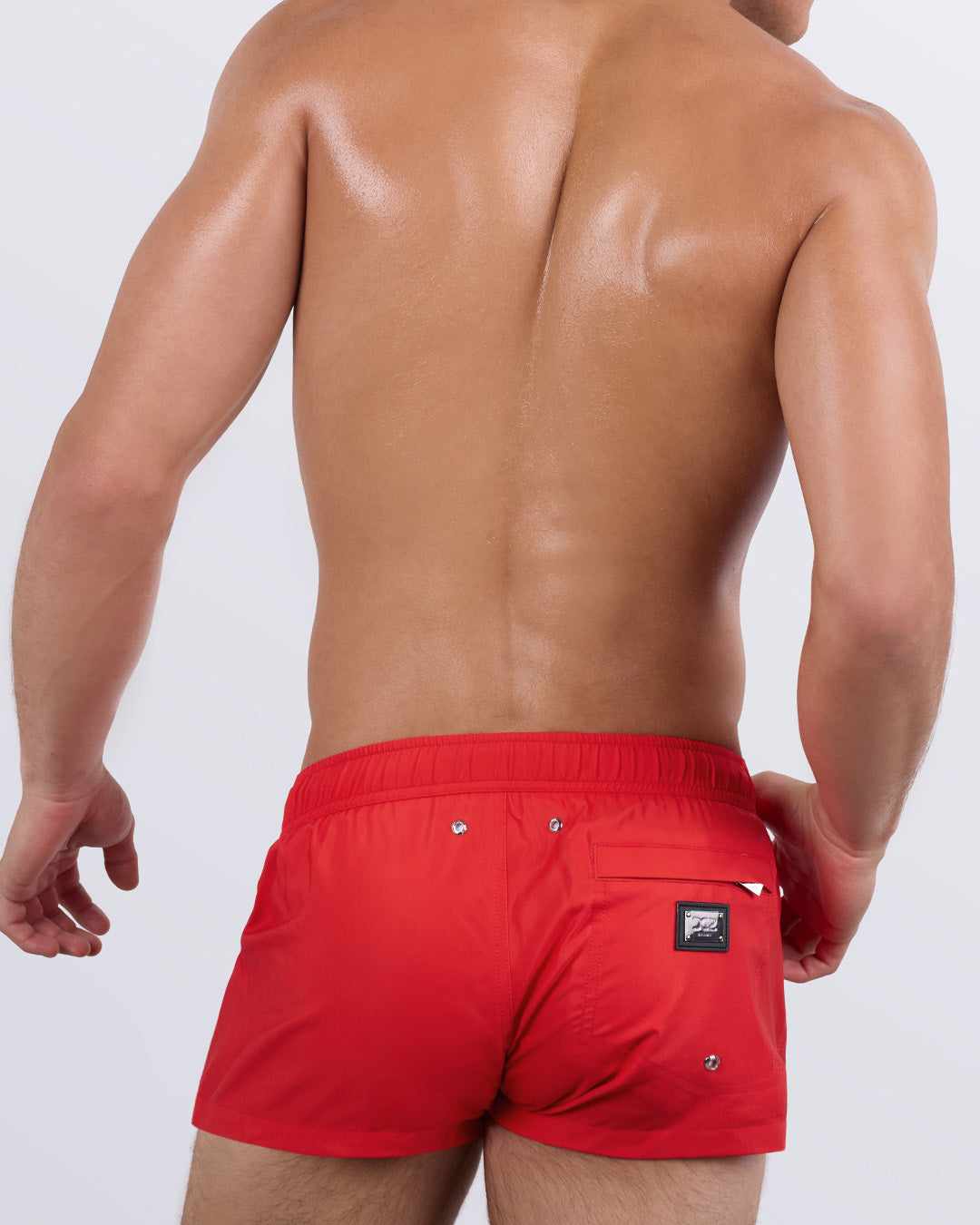 Back view of a male model wearing the men's PRIME RED Mini Shorts by DC2 Miami. Featuring a vibrant red design, a tailored ultra-short fit, and a functional back pocket with a DC2 signature metal logo plaque, these statement swim shorts offer both comfort and confidence.