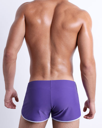 Back view of a male model wearing the PURPLE MACHINE beach Swim Shorts for men by DC2 Miami in a solid purple color.