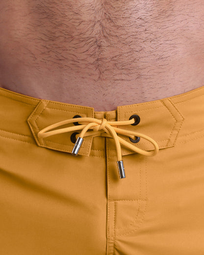 Close-up view of men’s summer Flex shorts by DC2 clothing brand, showing  yellow color cord with custom-branded golden cord ends, and matching custom eyelet trims in gold.