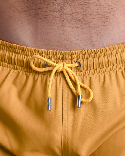 Close-up view of the RETRO MUSTARD men’s summer shorts, showing dark yellow cord with custom branded silver cord ends, and matching custom eyelet trims in silver.