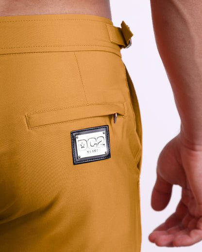 Close-up view of the RETRO MUSTARD men’s swimwear, showing custom branded silver metal logo.