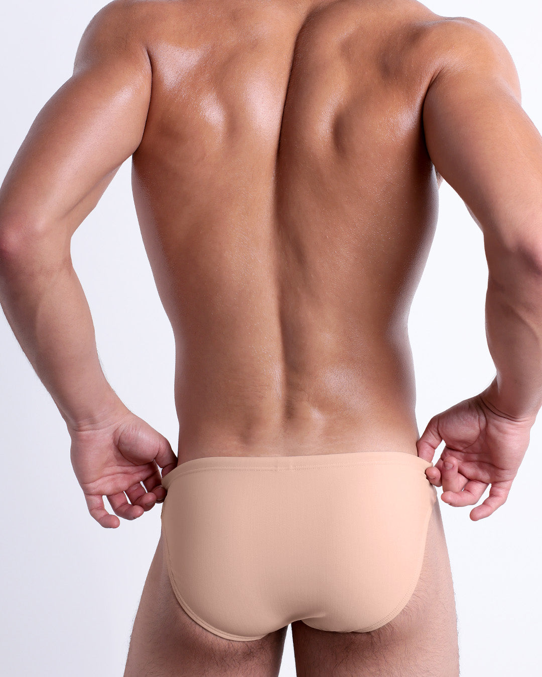 Back view of male model wearing the SKINNY DIP beach mini-briefs for men by DC2 Miami in a solid light cream color.