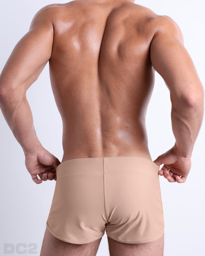 Back view of male model wearing the SKINNY DIP beach Swim Shorts for men by BANG! Miami in a solid tan color.