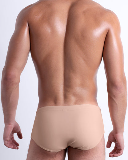 Back view of a male model wearing the SKIINY DIP beach Brazilian Sunga swimwear for men by BANG! Miami in a solid light cream color.