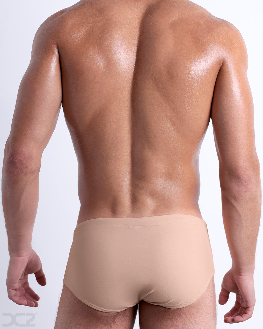 Back view of male model wearing the SKIINY DIP beach Brazilian Sunga swimwear for men by BANG! Miami in a solid light cream color.