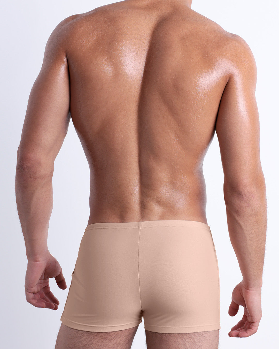 Back view of a male model wearing the SKINNY DIP men’s swim trunks by DC2 Miami in a solid pale tan color.
