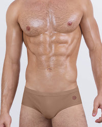 Male model wearing DC2 Miami SKINNY DIP (TAN) swim briefs in a matte tan nude tone, designed with a low-rise fit and sculpted pouch for beach and pool wear.