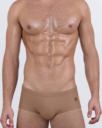 Male model wearing DC2 SKINNY DIP (TAN) swim sunga with smooth matte finish and minimalist logo detail at the hip.
