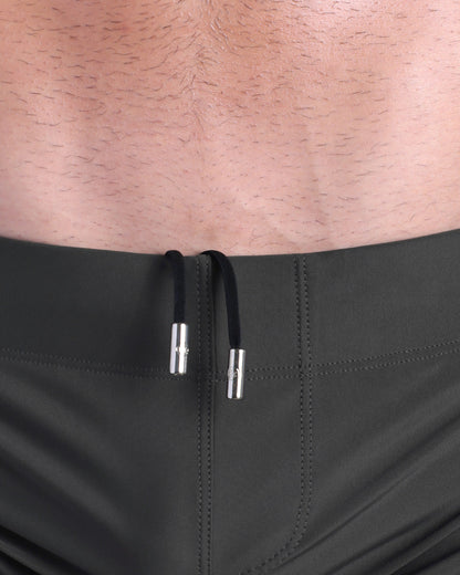 Close-up view of men’s summer beach shorts by DC2 clothing brand, showing black cord with custom branded metallic silver cord ends.