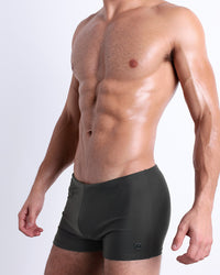DC2 SLIM GREEN Swim Trunks — model wearing slim-fit square-cut swim trunks in muted olive green, featuring a snug silhouette.