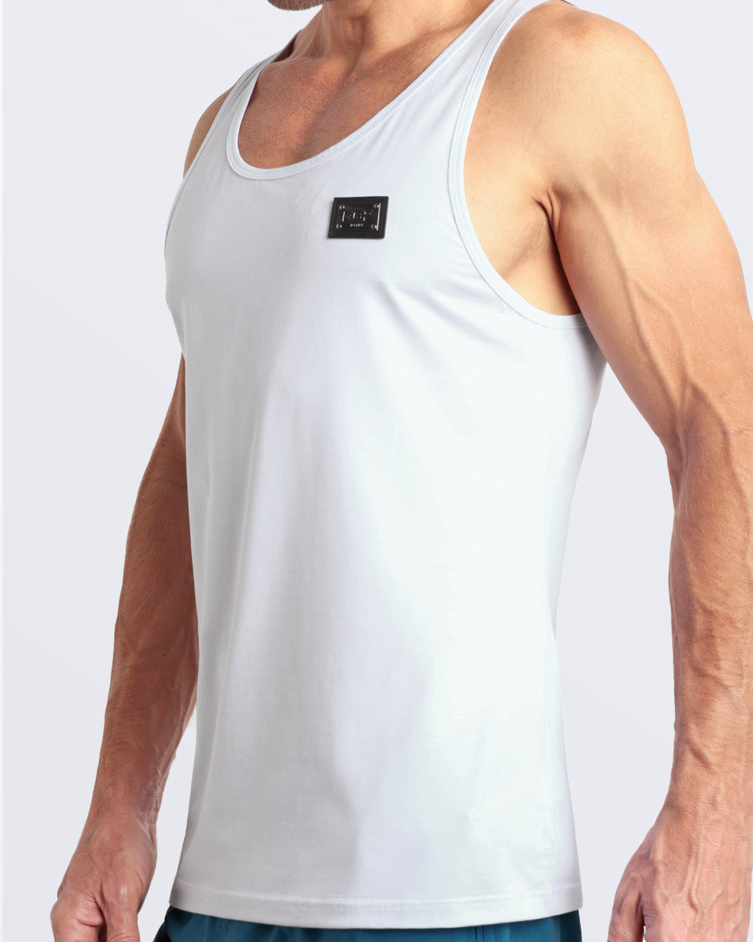 Side view of men’s workout tank top in SOFT WHITE a light cream white color with a metallic plaque logo made by DC2 Clothing the new official brand of mens beachwear.