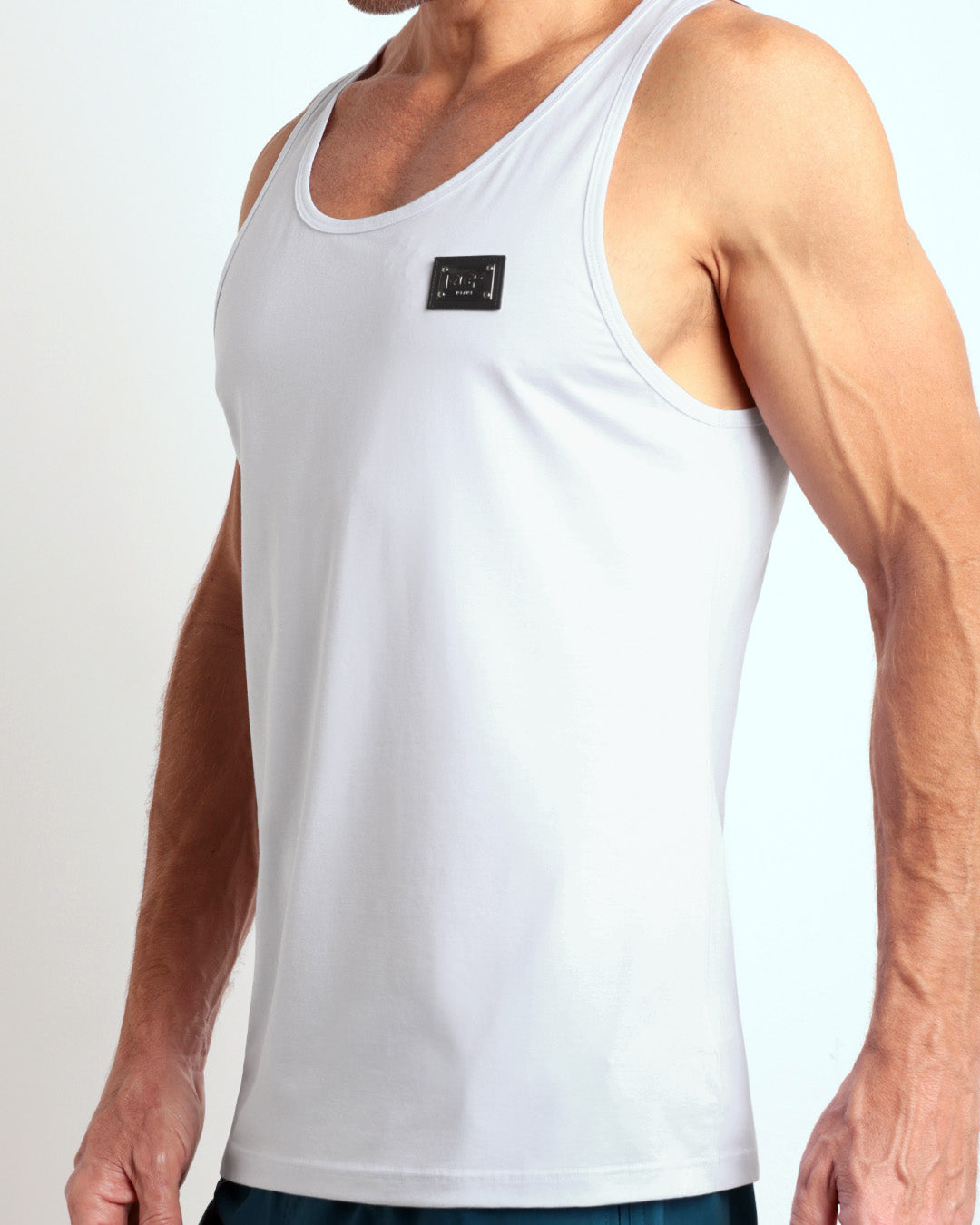 Side view of men’s workout tank top in SOFT WHITE a light cream white color with a metallic plaque logo made by DC2 Clothing the new official brand of mens beachwear. 