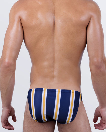 Back view of SUN CHASING STRIPES men's swim mini briefs featuring clean vertical lines in golden yellow and white on a deep navy canvas. A daring, low-cut design crafted in 4-way stretch fabric for all-day resort comfort.