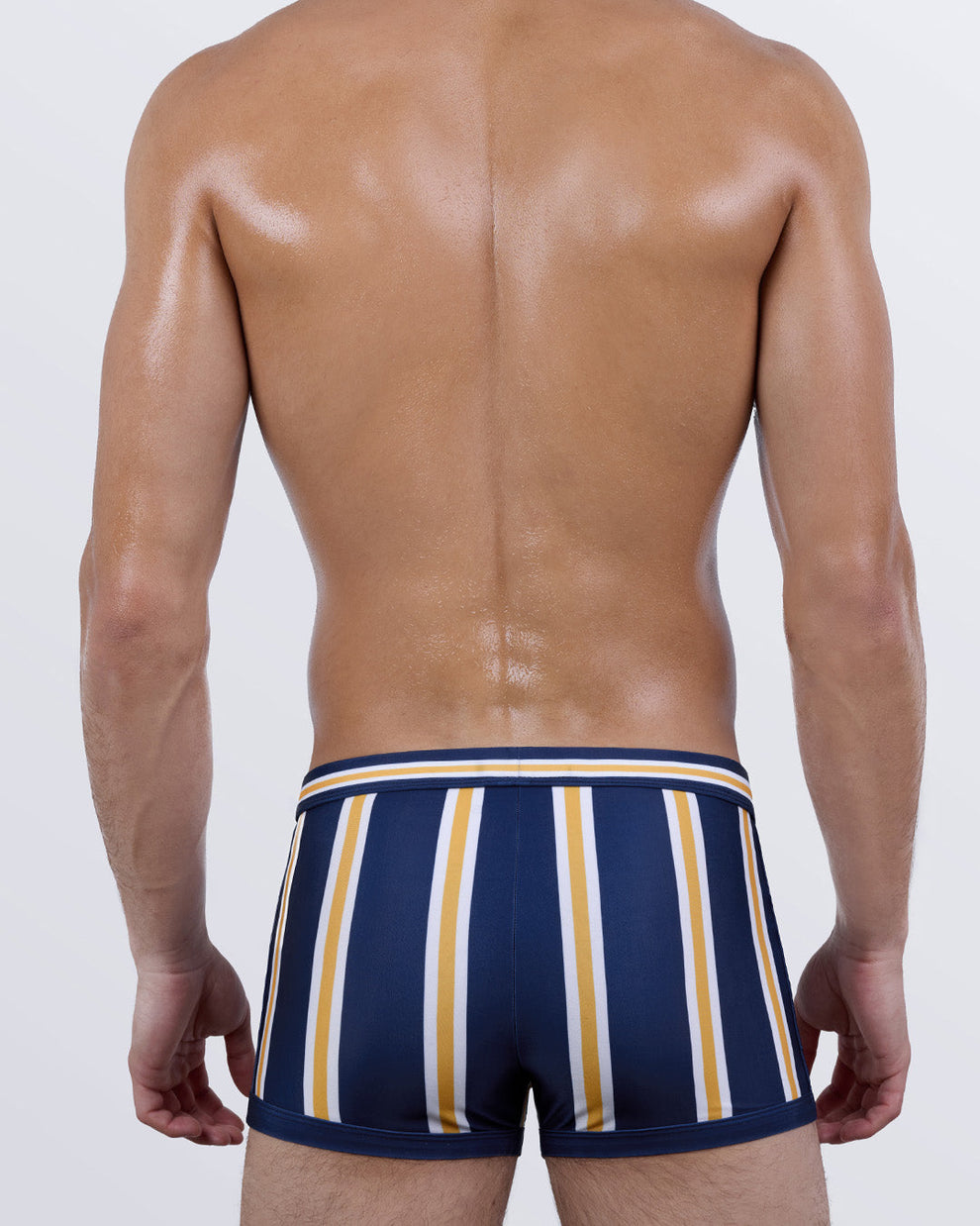 Back view of SUN CHASING STRIPES men's swim trunks showcasing curve-enhancing fit and vertical stripe pattern in navy, white, and yellow. Designed for a sculpted silhouette and elevated poolside look.