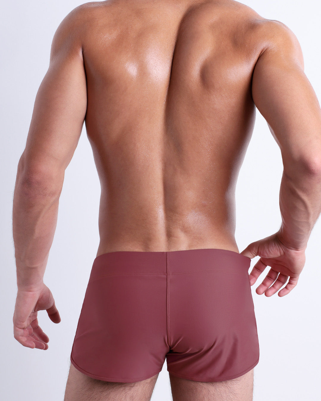 Back view of a male model wearing the SUNKISSED RED beach Swim Shorts for men by BANG! Miami in a solid blush color.