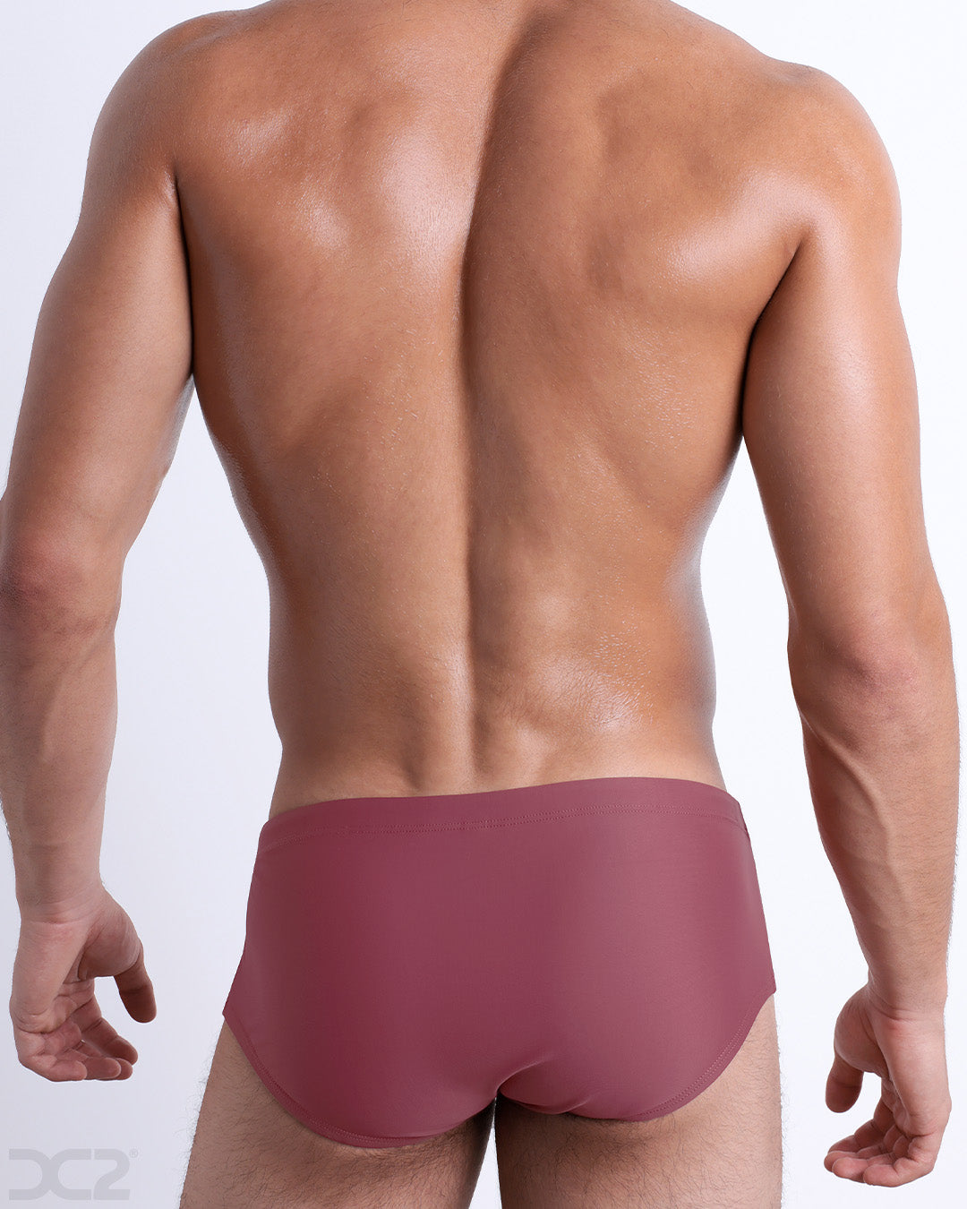 Back view of male model wearing the SUNKISSED RED beach Brazilian Sunga swimwear for men by BANG! Miami in a solid red color.