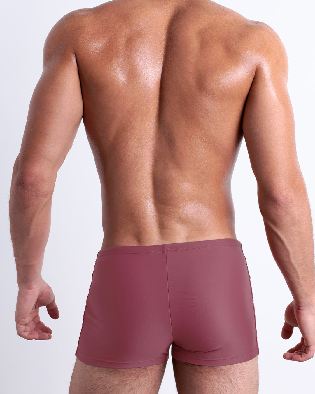 Back view of a male model wearing the SUNKISSED RED men’s swim trunks by DC2 Miami in a solid brick red color.