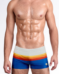 DC2 Sunset Stripes — model wearing Sunset Stripes Swim Trunks featuring soft beige waistband with horizontal sunset bands in yellow, orange, red, and deep blue.