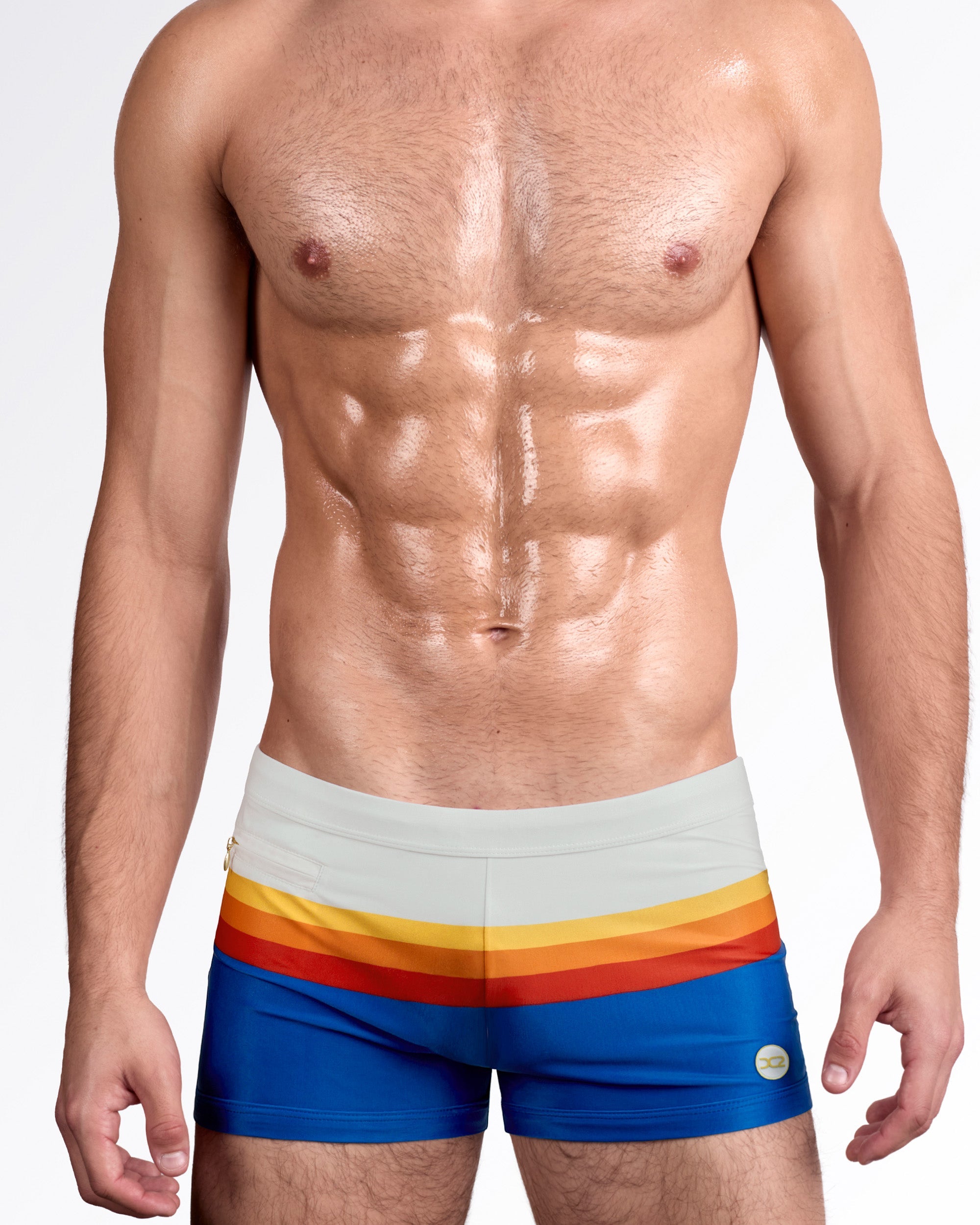 DC2 Sunset Stripes — model wearing Sunset Stripes Swim Trunks featuring soft beige waistband with horizontal sunset bands in yellow, orange, red, and deep blue.