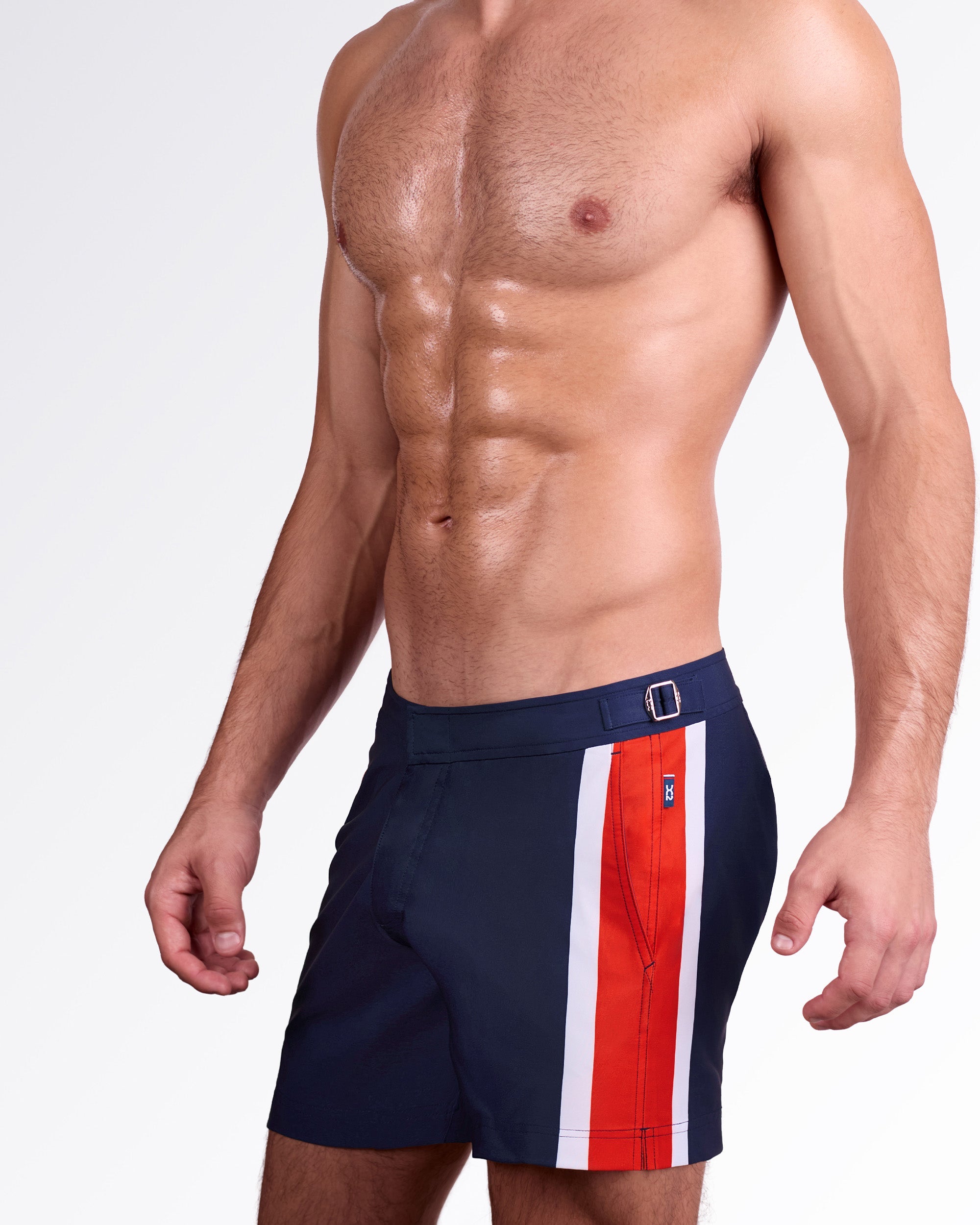DC2 Miami Maritime Tailored Shorts — model wearing men’s tailored swim shorts in navy blue with vertical red and white side stripe, featuring structured waistband with side adjusters and a clean tailored fit.