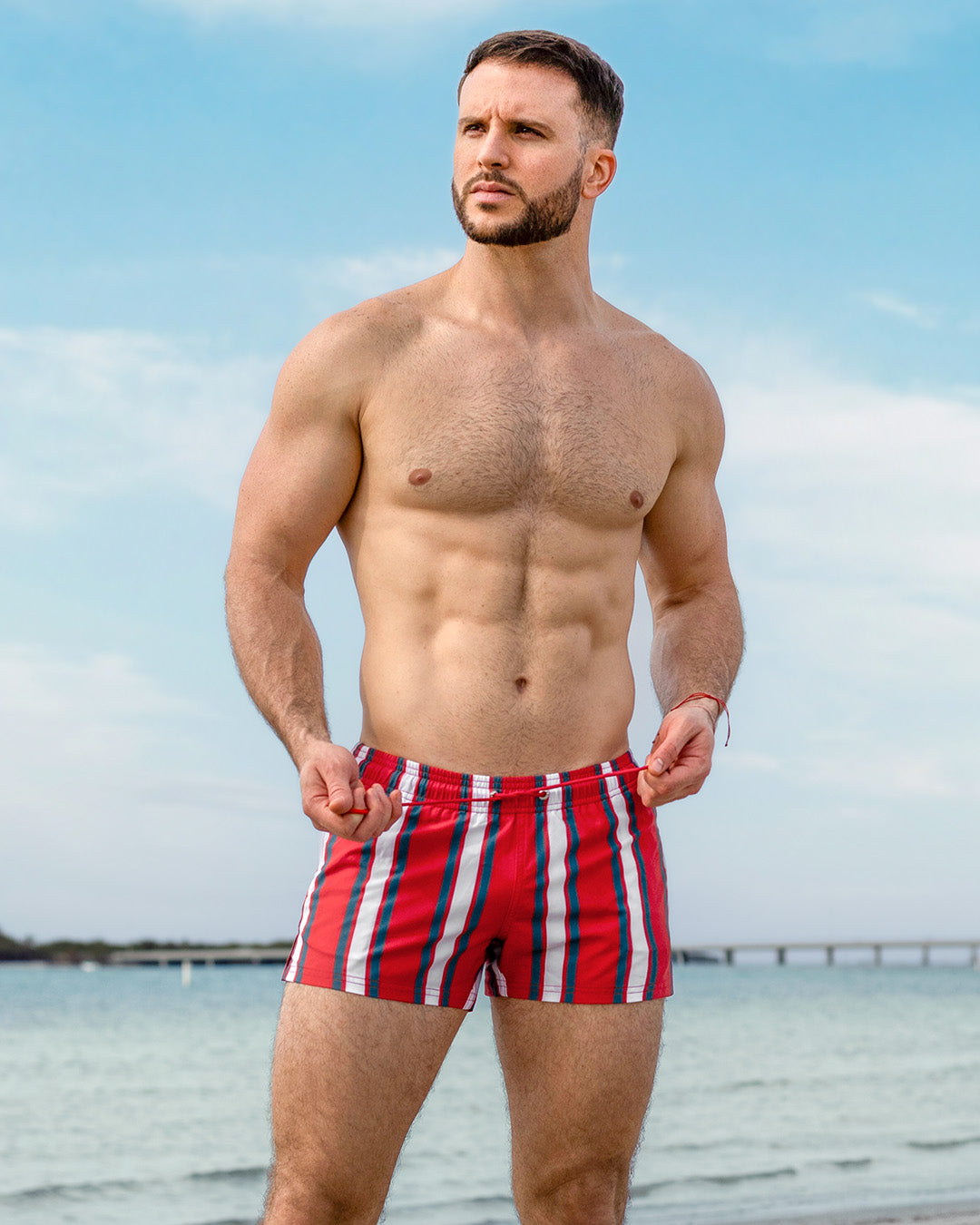 DC2 Swift Stripes Poolside Shorts — model wearing red, white, and teal striped swimming beach shorts with a tailored fit, crafted in quick-dry fabric for sleek seaside style.