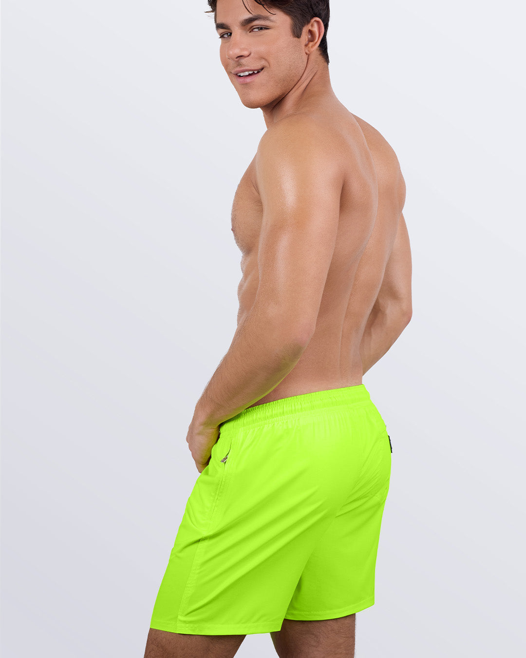 Back view of a male model wearing the ULTRA NEON Resort Shorts by DC2 Miami, smiling confidently over his shoulder. These stylish swim shorts feature a relaxed, breathable fit, an elastic waistband, and a premium fabric blend, making them perfect for lounging, swimming, or resort getaways.