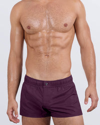 Frontal view of a masculine model wearing the VERY BERRY Mini Shorts for men by DC2 Miami, a premium swimwear brand. These ultra-short beach shorts feature a rich berry purple color, an elastic waistband with an adjustable internal drawstring, and a sleek fitted cut, making them perfect for stylish summer looks, beach outings, and poolside lounging.