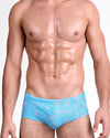 DC2 Viva La Vida (En Rose) — model wearing Viva La Vida En Rose Swim Sunga featuring a vibrant aqua base with soft pink illustrated icons and script details in a sleek, body-contouring silhouette.