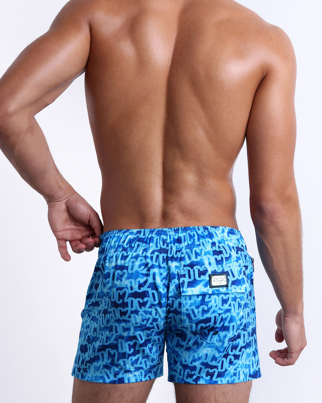 Back view of a male model wearing men’s WET Flex Shorts swimsuits featuring a monogram print of the DC2 logo print designed by DC2 a brand based in Miami.